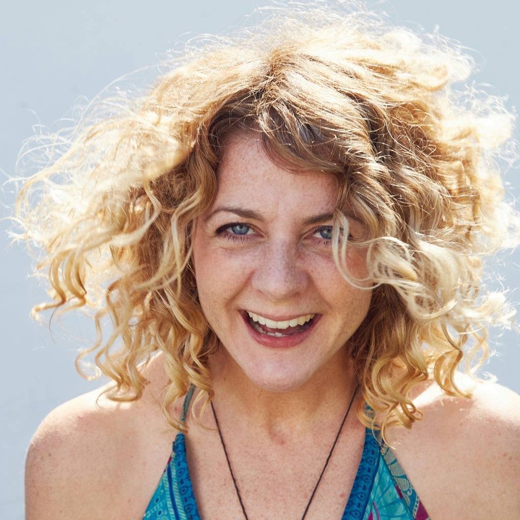 A smiling woman with curly blond hair, photographed in bright light
