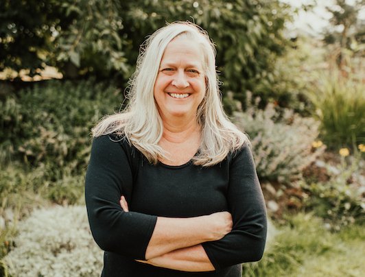 Portrait of Susan Bennett Fisher outdoors, arms crossed, smiling