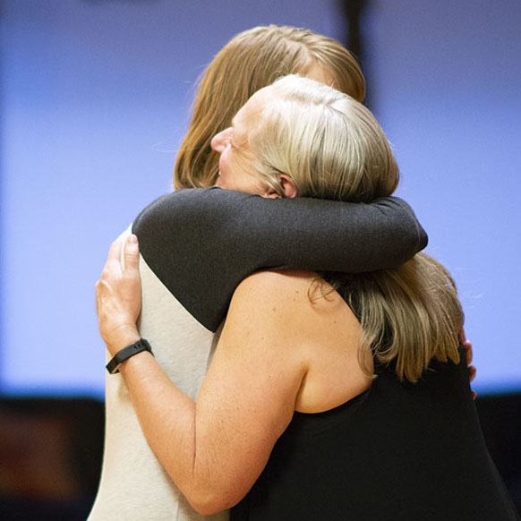 Two women sharing a warm embrace on a softly lit stage